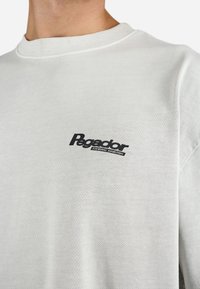 Light gray cotton sweatshirt featuring a ribbed neckline and a black logo on the left chest. Smooth texture with a relaxed fit.
