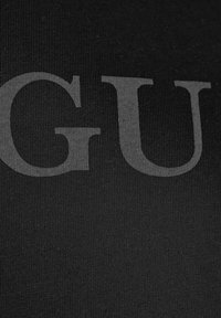 Czarna tkanina z wyraźnym, dużym nadrukiem "GU" w tonacji. Tekstura jest gładka z prążkowanym wyglądem.