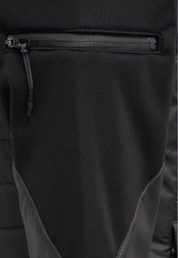 Svarta träningsbyxor med ett slätt tyg som har en texturerad panel, samt en liten dragkedjeficka på baksidan.