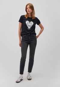 Schwarzes Baumwoll-T-Shirt mit einem weißen Grafikdruck von zwei Gesichtern in Herzform. Kombiniert mit hoch taillierten dunklen Jeans und Sneakern.