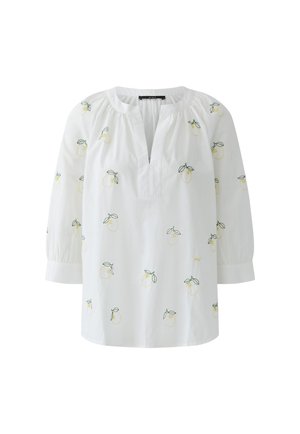 Weiße Bluse mit 3/4-Ärmeln, offenem V-Ausschnitt und kleinen gelben Zitronenmuster mit grünen Blättern, die über den Stoff verteilt sind.