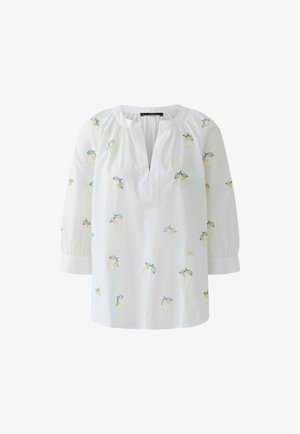 Weiße Bluse mit 3/4-Ärmeln, offenem V-Ausschnitt und kleinen gelben Zitronenmuster mit grünen Blättern, die über den Stoff verteilt sind.