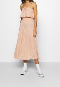 Robe maxi sans bretelles en pêche avec un design à étages, un motif floral et un col à volants. Assortie à des baskets montantes blanches et des chaussettes.