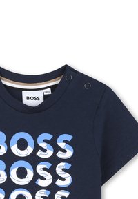 T-shirt in cotone blu navy a maniche corte con logo "BOSS" ripetuto in azzurro, arricchito da dettagli con bottoni a pressione sulla spalla.