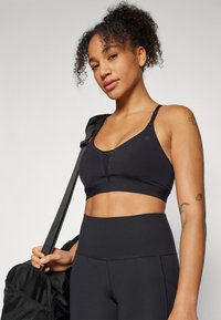 Sostenedor deportivo negro con diseño de escote en V, tirantes ajustables y paneles de malla. Combinado con leggings negros de cintura alta. Estética minimalista.