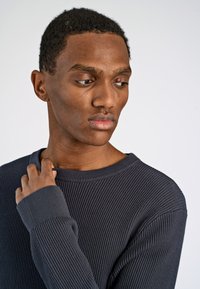 Maglione a costine grigio scuro con scollatura ampia e maniche lunghe, caratterizzato da un tessuto testurizzato e una silhouette aderente.