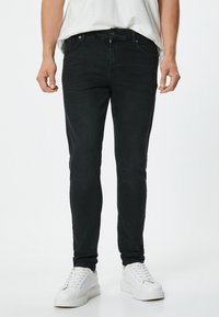 Mustat slim-fit farkut, joissa on klassinen 5-taskun malli, vyölenkit ja minimiset ompelusaumat. Yhdistetty valkoisiin lenkkareihin.