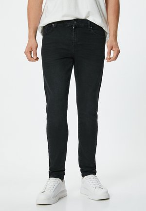 Jeans negros ajustados de mezclilla, con un diseño clásico de 5 bolsillos, pasadores para cinturón y mínimos detalles de costura. Combinados con zapatillas blancas.