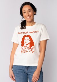 T-shirt en coton blanc avec une illustration graphique rouge d'une femme tenant de la nourriture, avec le texte "MARCHÉ DES AGRICULTEURS" au-dessus. Manches courtes, coupe décontractée.