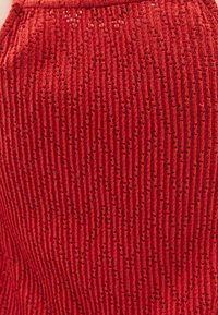 Tessuto di maglia rossa con righe verticali e piccoli fori, creando un motivo testurizzato. Il materiale sembra leggero e traspirante.