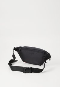 Schwarze Gürteltasche aus strapazierfähigem Stoff, mit Reißverschluss, verstellbarem Gurt und einem kleinen roten Akzent mit einem eingeprägten Logo.