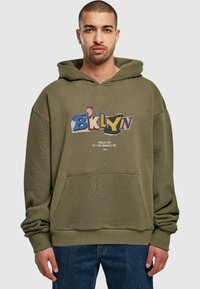 Olívazöld kapucnis felső, elülső zsebbel, amelynek grafikus szövege színesen van feltüntetve, és azt mondja: "BKLYN", alatta pedig egy kisebb szöveg található.