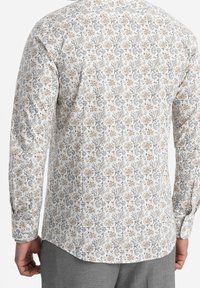 Langarmshirt met een bloemenpatroon in beige, grijs en blauw op een witte achtergrond, met een gebogen zoom en knopenmanchetten.