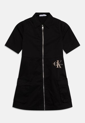 Zwarte jurk met korte mouwen, rits aan de voorkant, kraag, twee grote zakken en beige Calvin Klein Jeans-logo aan de rechterkant.