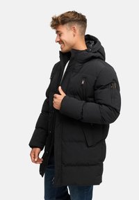 Chaqueta de abrigo negra con capucha, que cuenta con cierre de cremallera en la parte delantera, bolsillos laterales y puños elásticos. Textura suave con detalles de diseño acolchado.