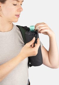 Schwarzer isolierter Wasserflaschenhalter, der an einem Riemen befestigt ist, mit einer klaren Flasche darin. Eine Person richtet den Kordelverschluss oben am Halter ein.