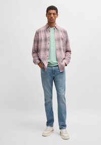 Camisa xadrez com botões em rosa e cinza, sobreposta a uma t-shirt verde menta. Combinada com jeans azul claro e ténis bege.