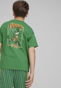 Maglietta in cotone verde con un personaggio dei cartoni animati che gioca a basket sul retro, con il testo "Puma" e "Sports". Fit casual e maniche corte.