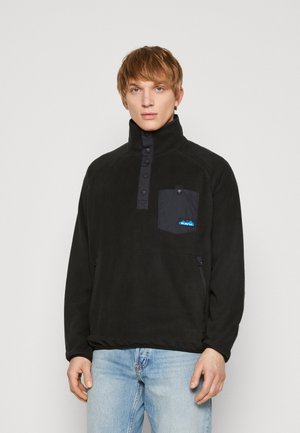 Pullover in pile nero con colletto alto, pattina con bottoni frontale, taschino sul petto in tessuto scuro e tasche laterali con zip.