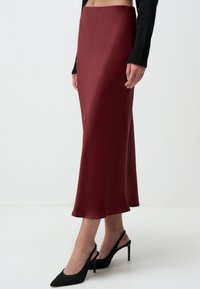 Gonna midi in satin bordeaux con una texture liscia e silhouette dritta, abbinata a décolleté nere a punta e a un maglione nero aderente.