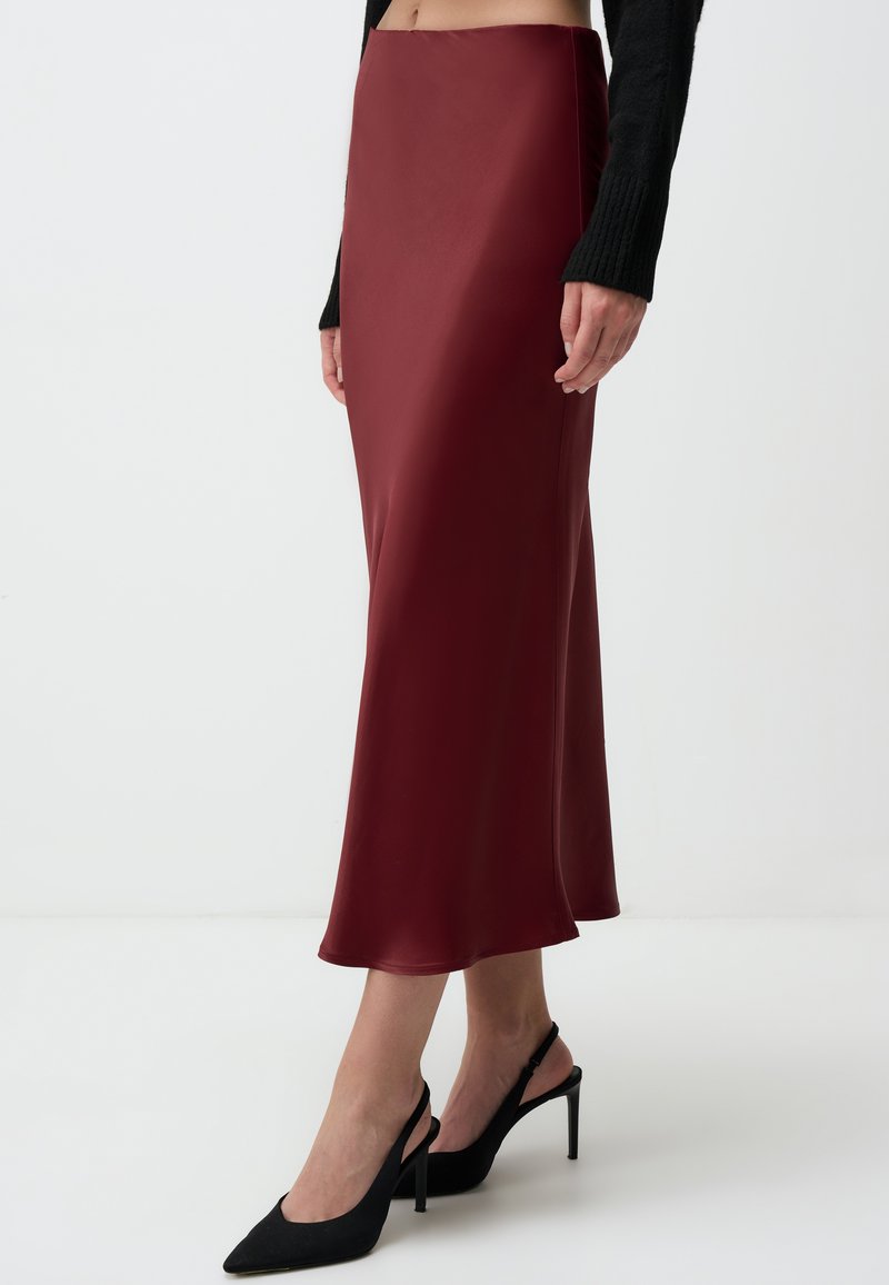 Gonna midi in satin bordeaux con una texture liscia e silhouette dritta, abbinata a décolleté nere a punta e a un maglione nero aderente.