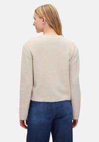 Beige texturerad pullovertröja med långa ärmar och rund halsringning, med en avslappnad passform och cropped nederkant. Denimbyxor syns nedanför.
