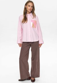 Roze gestreepte lange mouwen shirt met een pailletten zakdetail. Gepaard met brede bruine broeken. Soepele stof, relaxte pasvorm en knoopsluiting.