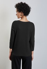 Schwarzes, geripptes Top mit einem runden Rückenausschnitt, Dreiviertelärmeln und lässiger Passform. Glatte Textur, minimalistisches Design.