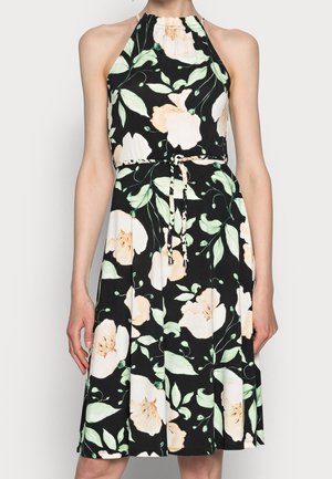 Mouwloze halterjurk met een zwarte achtergrond, grote witte en perzikkleurige bloemenprint, en een gevlochten taillekoord die vooraan is geknoopt.