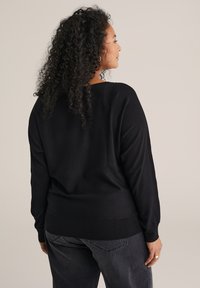 Fekete, laza szabású pulóver, bordás mandzsettával, széles nyakkivágással és textúrált anyaggal, sötétszürke, laza szabású nadrággal párosítva.