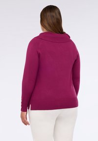 Jersey de color fucsia con cuello de barco, mangas largas, puños acanalados y aberturas laterales. Textura suave con botones dorados en las mangas.