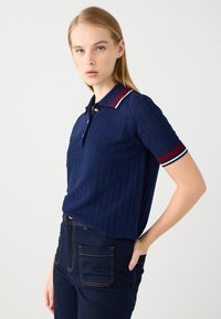 Polo a maniche corte blu navy con un motivo testurizzato, dotato di una patta con bottoni, colletto a righe bianche e rosse e dettagli a contrasto sulle maniche.