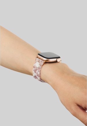 Ruusukultakuorinen älykello, jossa on läpinäkyvä vaaleanpunainen ja valkoinen hartsinen rannekkeiden linkki, ranteessa harmaata taustaa vasten.