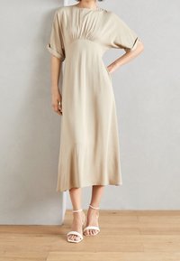 Beige midi šaty s volným střihem, krátkými ohrnutými rukávy a nařasením v pase. V kombinaci s bílými sandály na kotníkovém pásku.