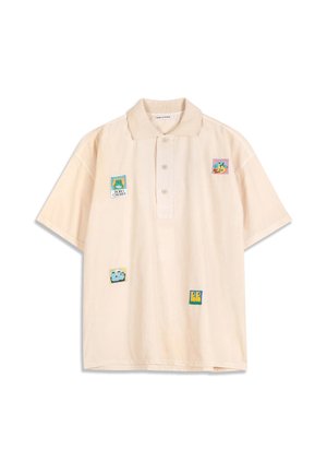 Lichtbeige polo met korte mouwen en vier kleurrijke vierkante patches met abstracte en cartoonontwerpen op de voorkant.