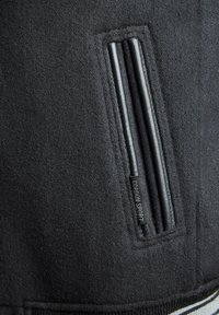 Black fleece jacket detail featuring a slim, vertical zippered pocket with textured black fabric and a branded label "Cordon Sport."