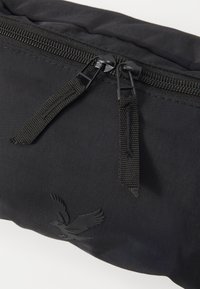 Borsa nera in nylon con chiusura a zip a doppio cursore, superficie texturizzata e logo di aquila in rilievo sul davanti.