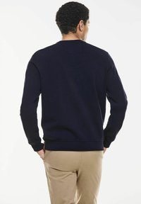 Mörkblå sweatshirt med långa ärmar, ribbade ärmslut och rundad halsringning. Mjukt tyg med minimala designdetaljer, visad från baksidan.