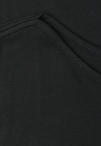 Gros plan d’un tissu noir avec des coutures visibles et des bords pliés montrant la texture et les détails des coutures.