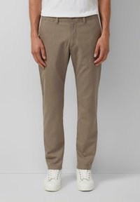 Beige gewobene Chinos mit geradem Schnitt, ausgestattet mit Fronttaschen, einem Knopfverschluss an der Taille und einer subtilen Textur. Kombiniert mit weißen Sneakers.