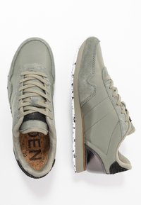 Baskets grises en matériaux suède et synthétiques, avec un talon noir texturé, des lacets gris clair et une semelle blanche et noire tachetée.