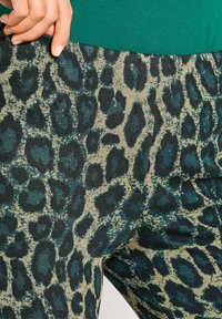 Luipaardprint legging in groen en beige, met een gestructureerde stof. Close-up weergave, die het onderscheidende patroon en de materiaaldetails laat zien.