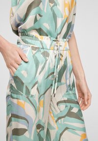 Lehký vzorovaný overal v mátově zelené, béžové a žluté barvě. Má elastický pas, kapsy a stahovací šňůrku s kovovým detailem.