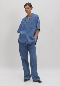 Jeanshemd en broekset in blauw, met een relaxte pasvorm, korte mouwen, borstzak en knopen. Het materiaal heeft een gladde textuur.
