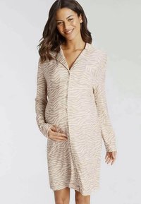 Chemise de maternité en doux tissu beige avec un imprimé zèbre. Présente des manches longues, une fermeture par boutons et une poche à l'avant.
