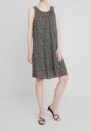 Robe sans manches à motifs noir et blanc, longueur genou, portée avec des sandales noires à brides et talons bas sur un mannequin debout.