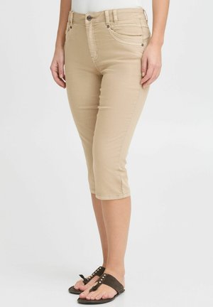 Jeans capri beiges avec une coupe ajustée, présentant une taille mi-haute, cinq poches et des détails de couture subtils, associés à des sandales à glissière marron.