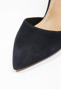 Chaussure à talon haut en daim bleu marine à bout pointu avec doublure intérieure beige sur fond blanc.