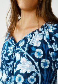 Blusa floreale blu con collo arricciato, caratterizzata da motivi di foglie e fiori bianchi su uno sfondo navy, realizzata in tessuto leggero.
