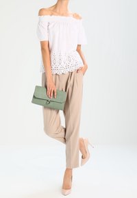 Vit av axlarna-top med spetskant, beige veckade byxor, rosa klackar och en grön clutch. Släta texturer och enkel design.